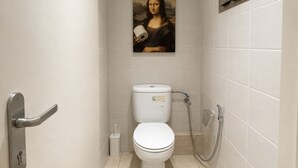 A bathroom with a toilet, a shower, and a painting of the Mona Lisa on the wall. - The Olive Flat (Rabat)