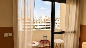 Un balcón con vistas a edificios, una pequeña mesa redonda con una silla y una lámpara en una mesita de noche.