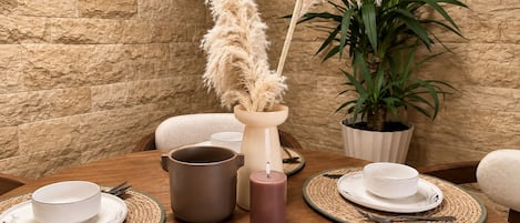 Une table à manger dressée avec des assiettes, des bols et des couverts, agrémentée d’un vase contenant des plumes d’herbe des pampas et d’une plante en pot.