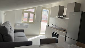 Una cocina compacta con sofá gris, una mesa de comedor y un refrigerador.