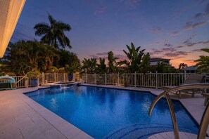 A swimming pool with a white fence, surrounded by palm trees and a sunset sky. - Matlacha Isles Waterfront - Pool, Spa & Tiki Bar (Matlacha Isles-Matlacha Shores)