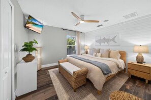 Quarto com cama, ventoinha no teto, televisão e janela com persianas.