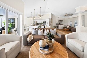 Ampla sala de estar com um sofá grande, uma mesa de centro com objetos decorativos e vista para a cozinha ao fundo.