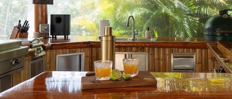 Una cocina con barra de madera, un fregadero y una parrilla. Hay dos vasos de una bebida amarilla en la barra, y una lima en la encimera.