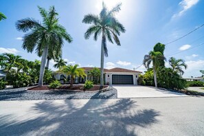 A residential property with a garage, palm trees, and a clear sky. - Matlacha Isles Waterfront - Pool, Spa & Tiki Bar (Matlacha Isles-Matlacha Shores)