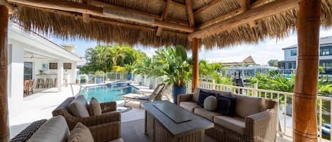 Un espacio de estar techado al aire libre con mobiliario de mimbre, una piscina y vistas del paisaje circundante.