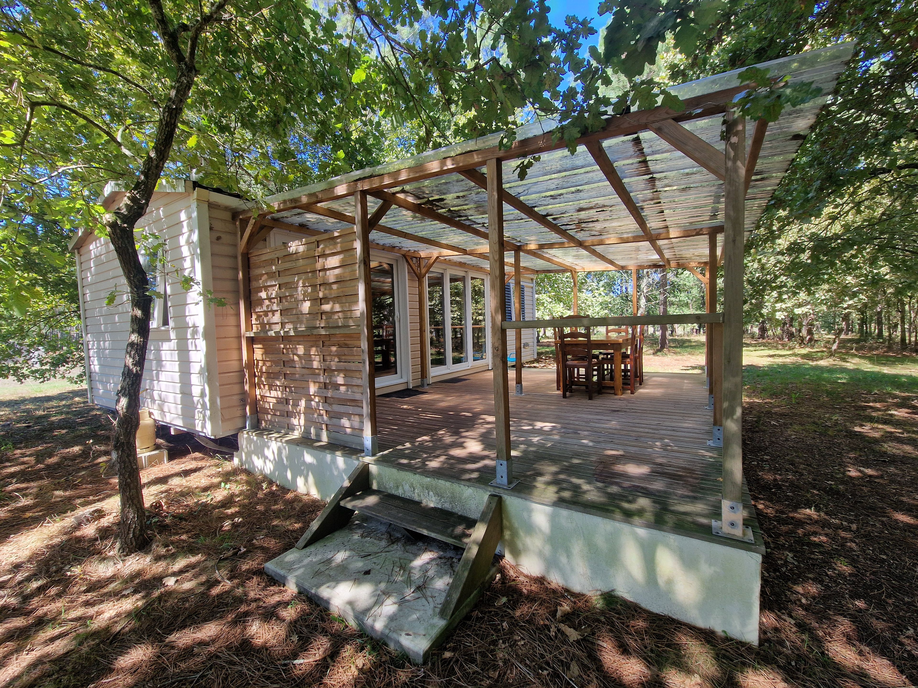 A covered wooden deck with a table and chairs, surrounded by trees and a house.