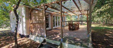 A covered wooden deck with a table and chairs, surrounded by trees and a house.