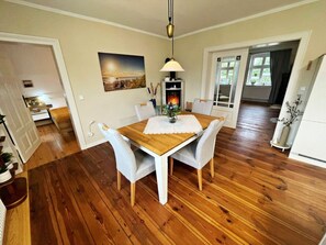 A dining area with a wooden table, white chairs, a pendant light, and a painting on the wall. - Holiday Home Anna (Benz)