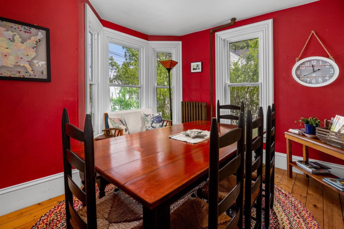 Comedor con mesa y sillas de madera, paredes rojas y ventana con vista a árboles.