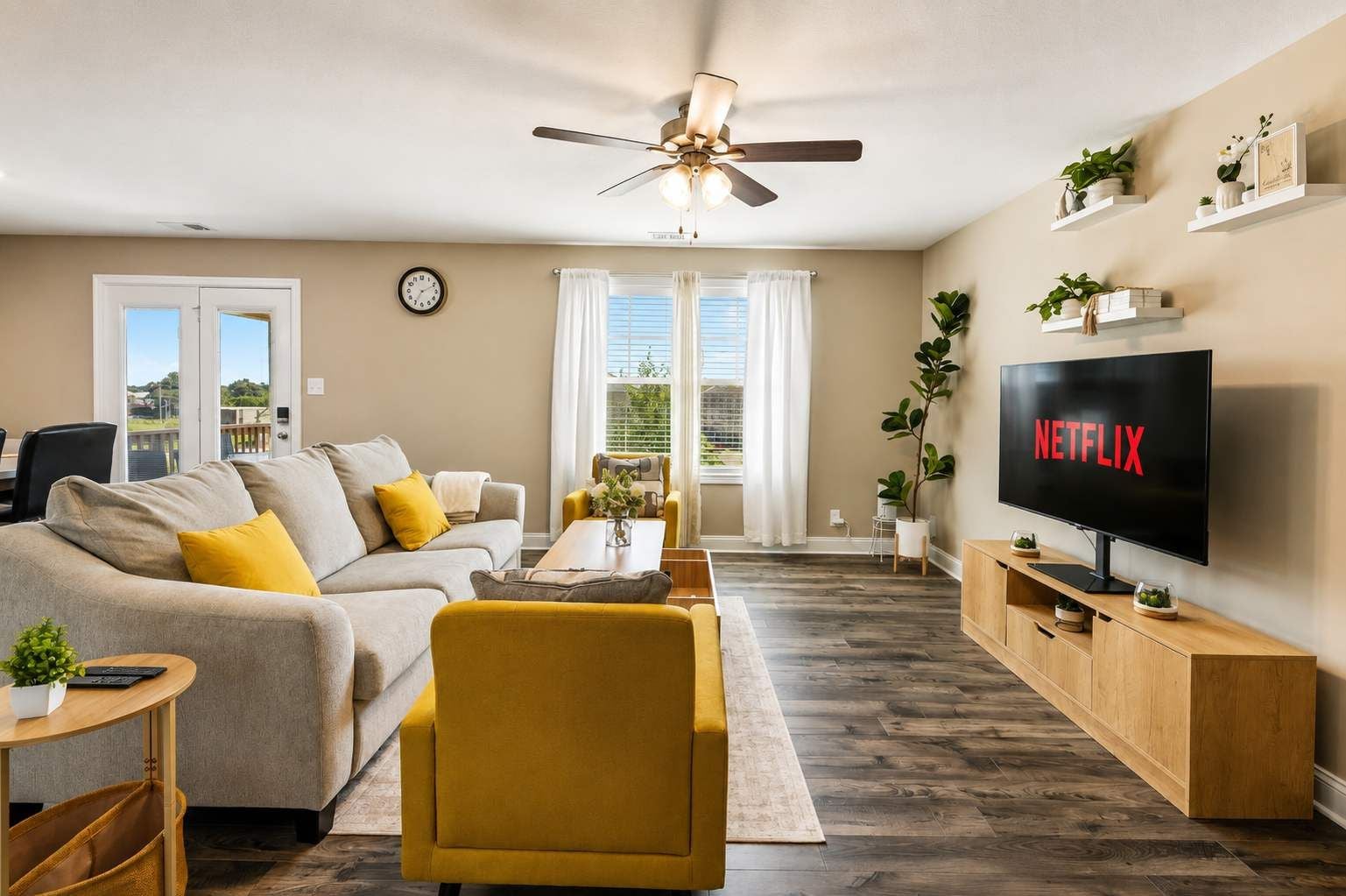 Una sala de estar moderna con sofá, sillón, mesa de centro, televisor y ventilador de techo.