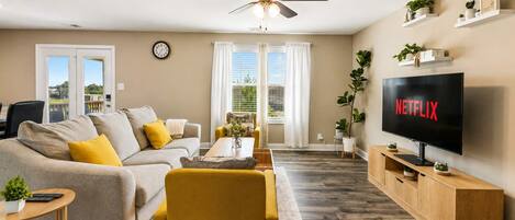 Una sala de estar moderna con sofá, sillón, mesa de centro, televisor y ventilador de techo.