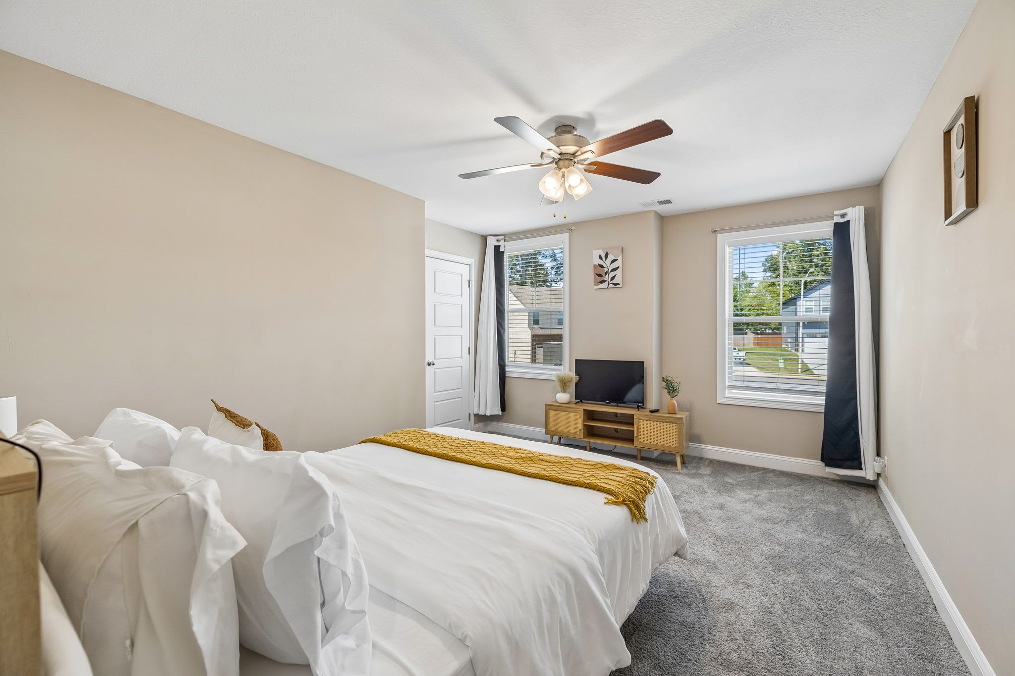 A bedroom with a bed, a television, a ceiling fan, and a window with curtains.