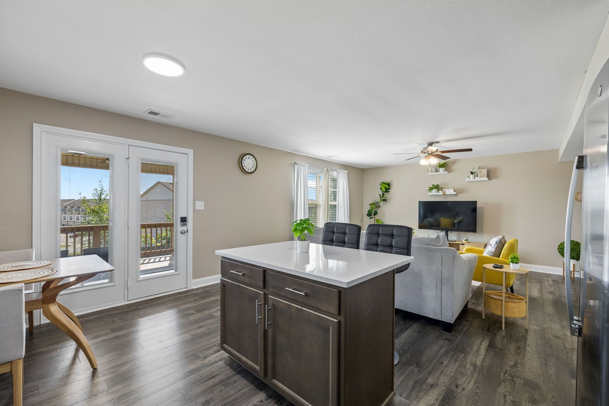 A modern kitchen with a central island, a dining area with a table and chairs, a living room with a sofa and a TV, and a balcony with a view.