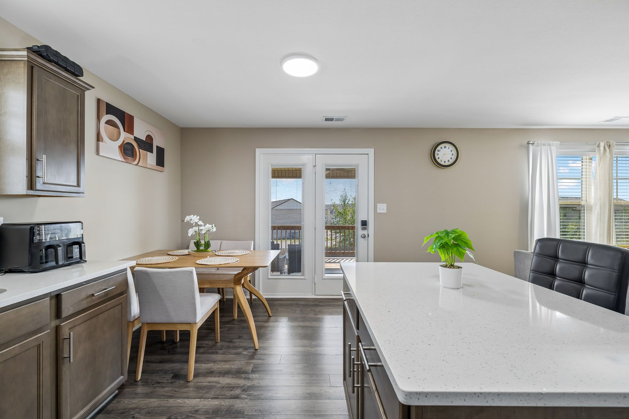 A modern kitchen with a central island, dining area, and a view through the glass doors.