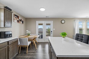 Una cocina moderna con una isla central, comedor y vistas a través de puertas de cristal.