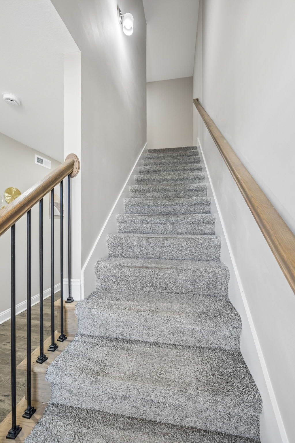 Un escalier avec une rampe en bois, une plateforme recouverte de moquette et un luminaire fixé au mur.