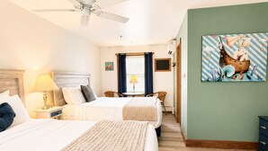 A hotel room with a bed, a ceiling fan, a nightstand, a lamp, a window with curtains, a wall painting, and a wooden floor. - Towne Motel Camben Room #13 (Camden)