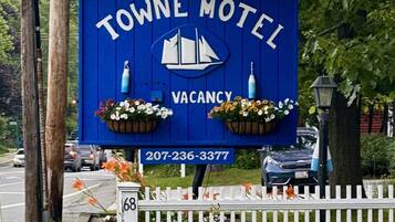 A blue sign for Towne Motel with a sailboat logo, indicating a vacancy, and a contact number.