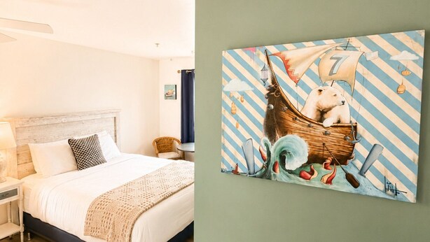 A bedroom with a bed, a nightstand, a lamp, and a wall-mounted painting of a polar bear in a boat. - Towne Motel Camben Room #13 (Camden)