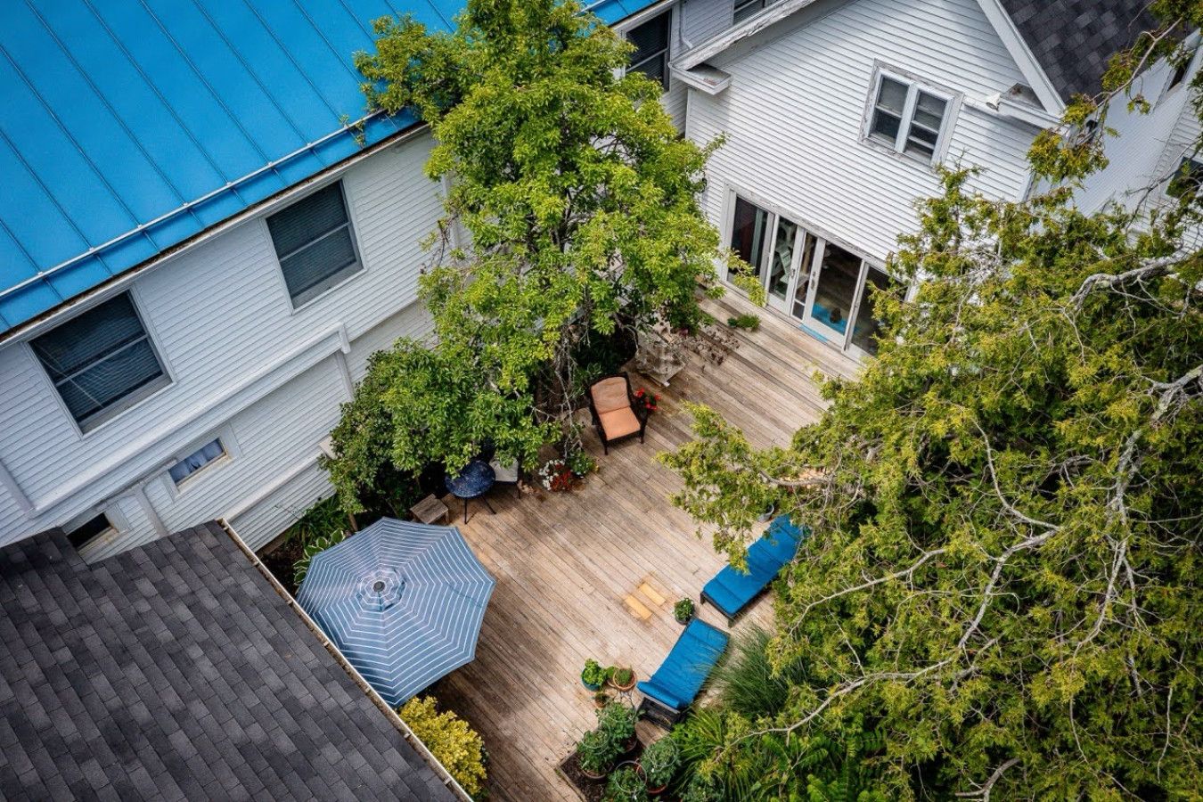 Una propiedad residencial con techo azul, terraza de madera y jardín con patio y asientos.