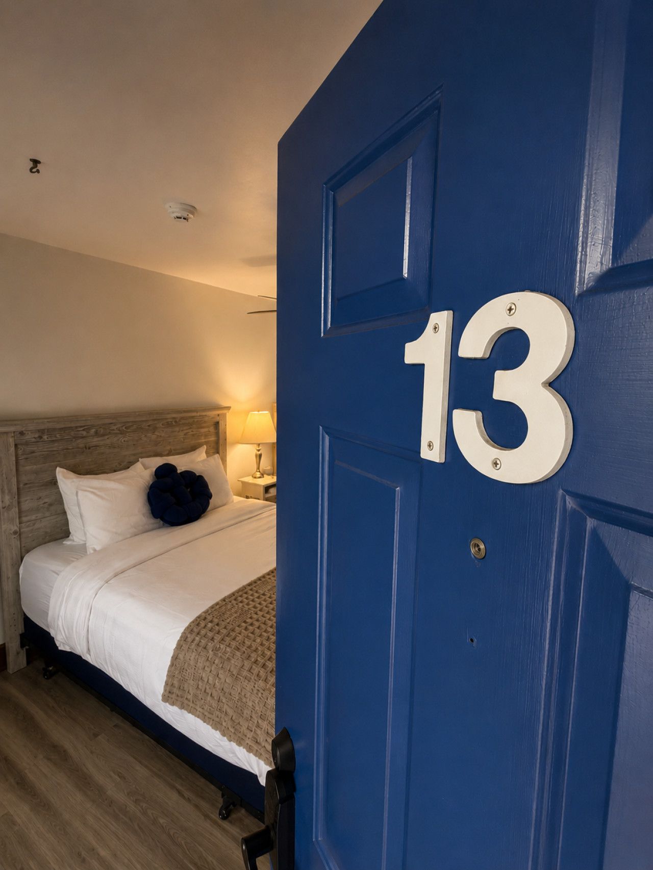 Ein Hotelzimmer mit einem Bett, einem Nachttisch, einer Lampe und einer blauen Tür mit der Nummer 13.