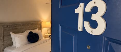 Et hotelværelse med en seng, et natbord, en lampe og en blå dør med nummer 13.