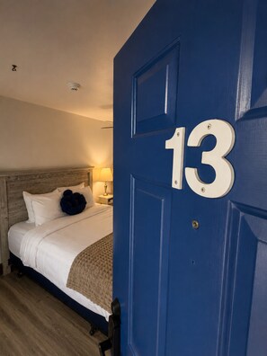 Habitación de hotel con una cama, una mesita de noche, una lámpara y una puerta azul con el número 13.