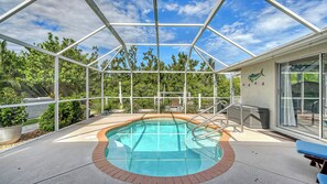 An outdoor swimming pool with a glass enclosure, surrounded by greenery and a clear sky. - Water Views | Beach | Pool | Paddle Boards (Bradenton)