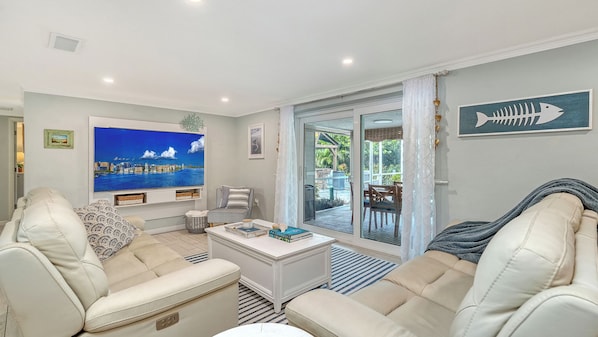 A living room with a large flat-screen TV, a sofa, a coffee table, and a view of the outdoors through a sliding glass door. - Water Views | Beach | Pool | Paddle Boards (Bradenton)