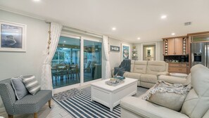 Ein modernes Wohnzimmer mit Glastür zum Balkon, ein beiges Sofa, ein gemustertes Sessel und ein weißer Couchtisch.