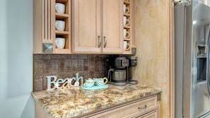 A kitchen with wooden cabinets, a granite countertop, a coffee maker, and a stainless steel refrigerator. - Water Views | Beach | Pool | Paddle Boards (Bradenton)