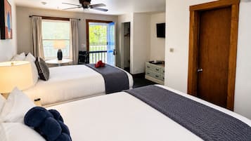 Ett hotellrum med två sängar, en takfläkt, ett fönster med gardiner, en trädörr och en byrå.