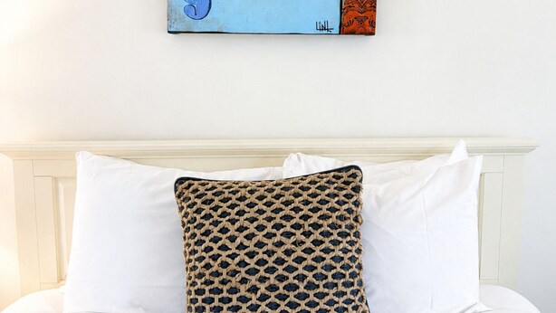 A bed with white bedding and a single decorative pillow with a woven pattern. - Towne Motel Camben Room #12 (Camden)