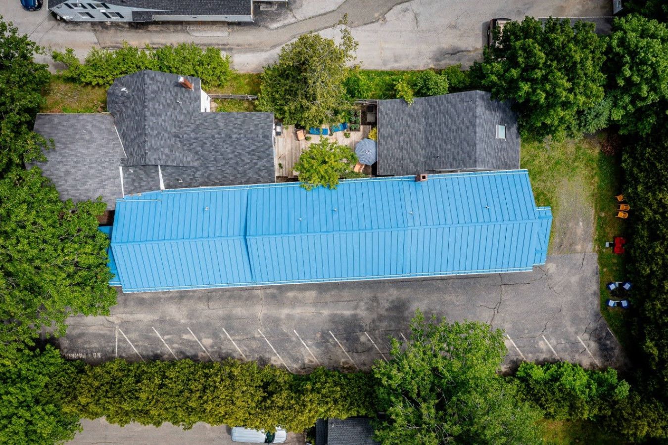 Un edificio grande con techo azul, rodeado de árboles y un estacionamiento.