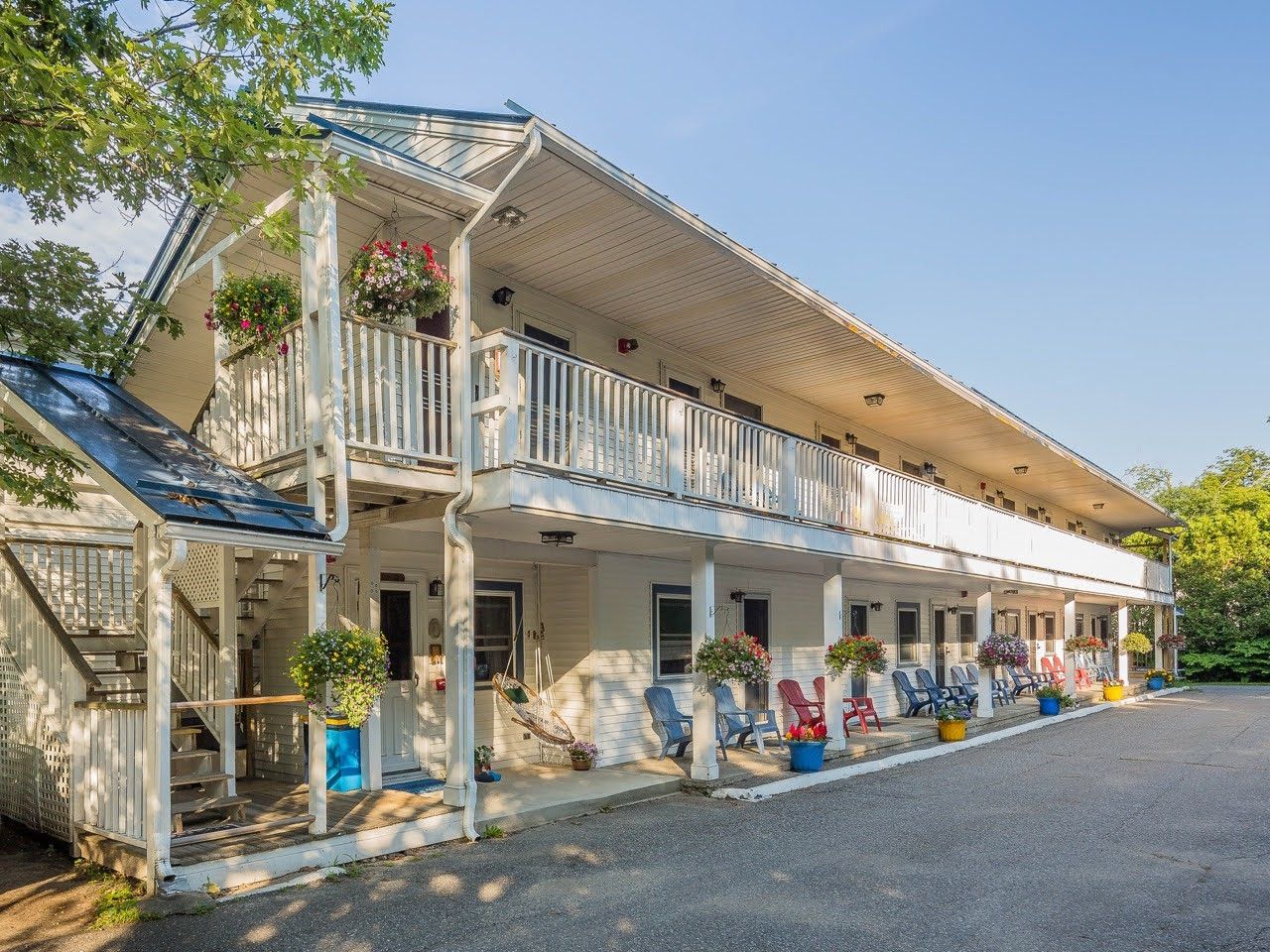 Ein zweistöckiges Gebäude mit einer Veranda, Sitzgelegenheiten im Freien und Topfpflanzen.