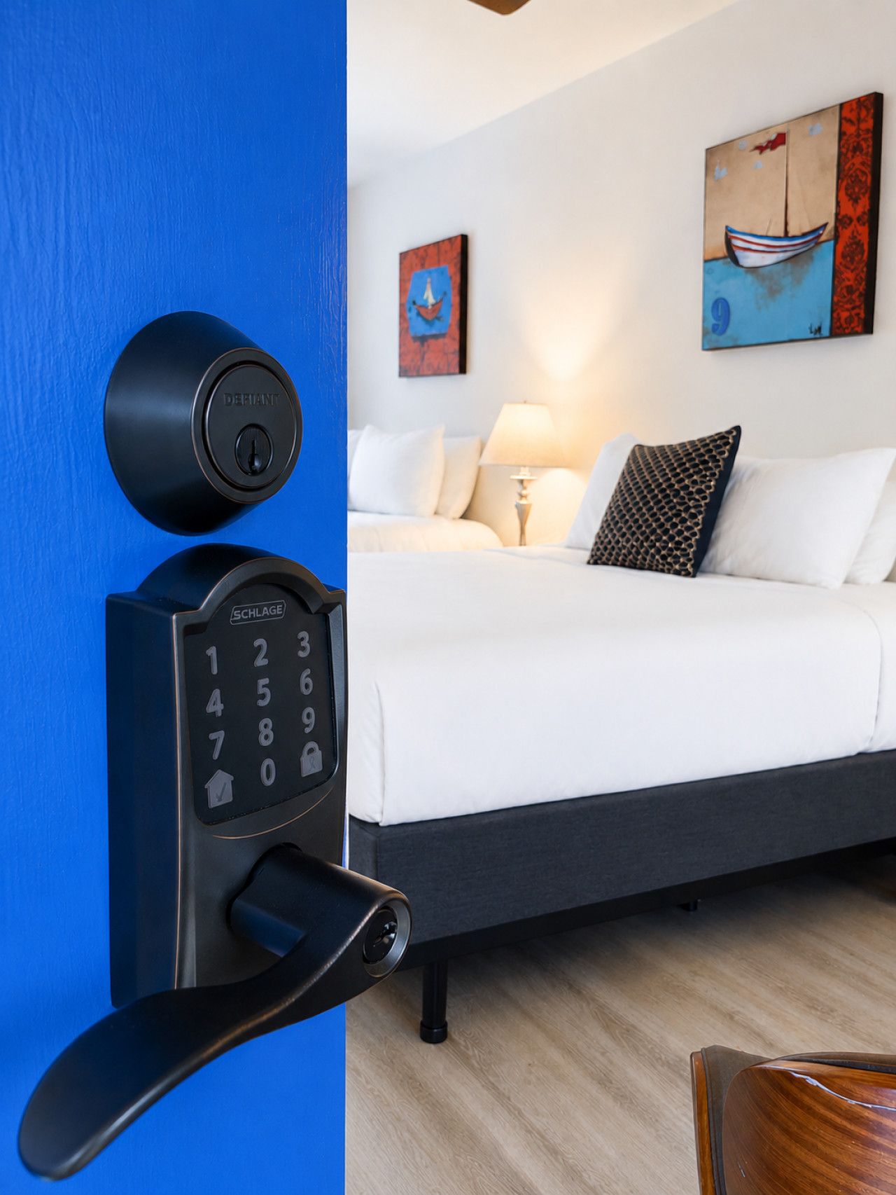 Habitación de hotel con una cama, una cerradura electrónica en la pared y un cuadro de un barco.
