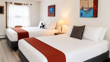 A hotel room with two beds, a window with curtains, a lamp, and artwork on the walls.