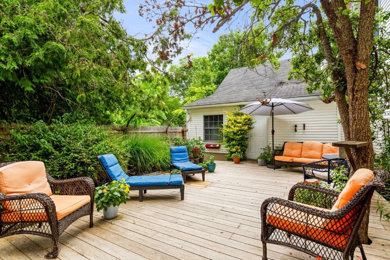 Un patio exterior con mobiliario de mimbre, una sombrilla y una casa al fondo.