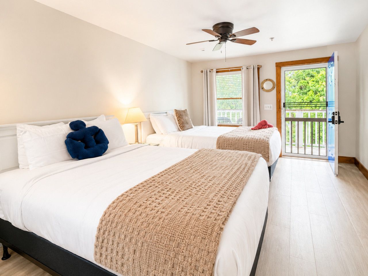 Habitación de hotel con dos camas, ventilador de techo, balcón con vistas y puerta al exterior.