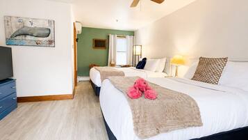 A hotel room with two beds, a ceiling fan, a painting of a whale, and a television on a dresser.