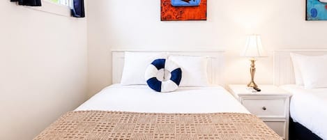 Et hotelværelse med en seng, et natbord, en lampe og to billeder på væggen.
