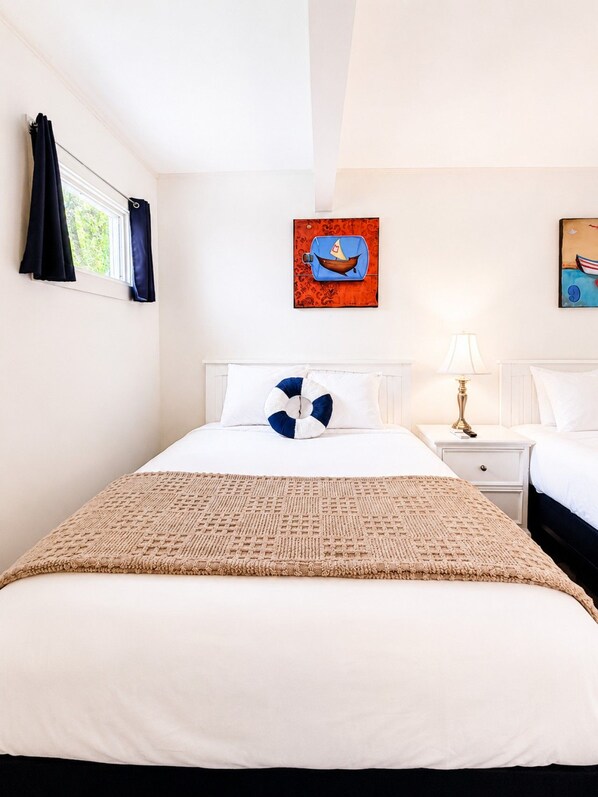 A hotel room with a bed, a nightstand, a lamp, and two paintings on the wall.