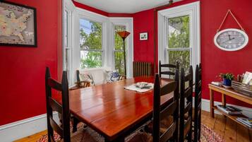 A dining room with a wooden table and chairs, red walls, and a window with a view of trees.