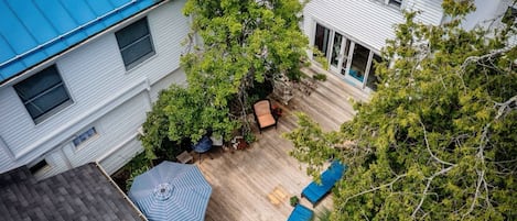 Una propiedad residencial con techo azul, terraza de madera y jardín con patio y asientos.