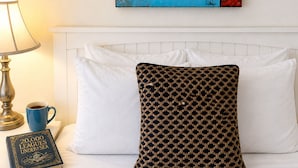 A neatly made bed with a patterned pillow, a book titled '20,000 Leagues Under the Sea,' a lamp, and a wall-mounted painting of a sailboat. - Towne Motel Camben Room #2 (Camden)