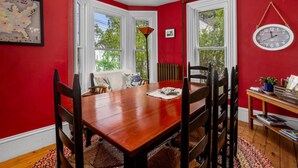 A dining room with a wooden table and chairs, red walls, and a window with a view of trees. - Towne Motel Camben Room #2 (Camden)