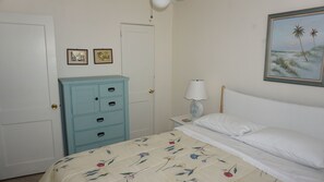 Une chambre à coucher avec un lit, une table de chevet avec une lampe, une commode et deux tableaux encadrés accrochés au mur.