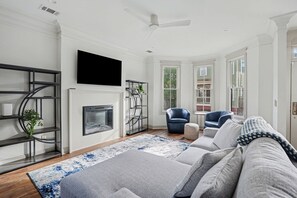 A living room with a fireplace, a flat-screen TV, a ceiling fan, and a large window. - Beautiful new construction just a walk to Starland Yard, local restaurants (Savannah)