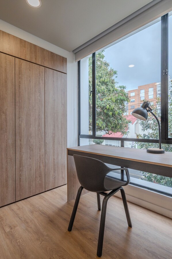 Un espacio de oficina moderno con un escritorio de madera, una silla y un ventanal con vistas a edificios y árboles.